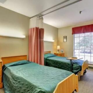 A hospital room with two beds separated by a curtain, featuring a window and standard healthcare furniture.