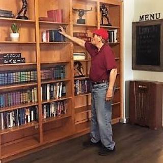 A person wearing a red cap and shirt selecting a book from a tall wooden bookshelf.