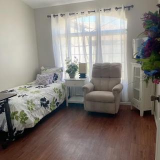 A cozy and bright room featuring a floral-patterned bedspread and a comfortable chair, illuminated by natural light.