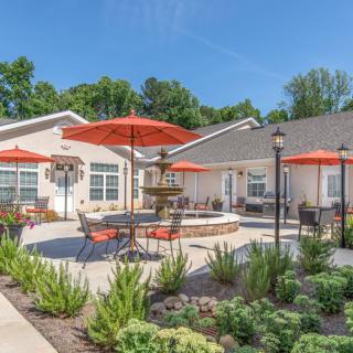 A beautifully landscaped courtyard featuring outdoor seating and a central fountain under red umbrellas on a sunny day.