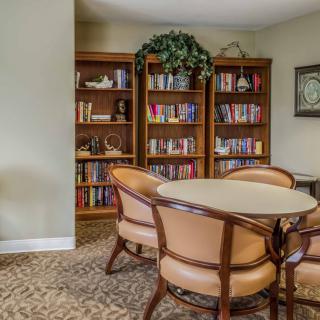 A cozy library room with bookshelves and a round table surrounded by chairs.