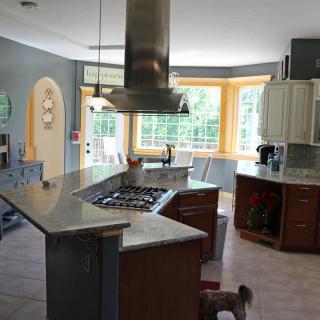 A modern kitchen with stainless steel appliances and a central island, featuring large windows and wooden cabinets.
