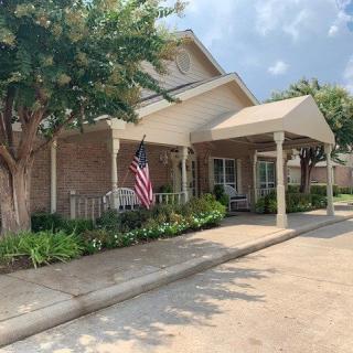 A brick residential house with a covered entrance and an American flag displayed, surrounded by trees and landscaping.