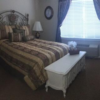 A cozy bedroom with a patterned bedspread, white furniture, and a window with curtains.
