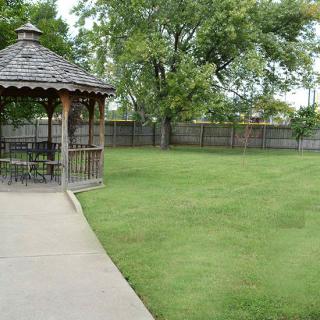 A peaceful outdoor setting featuring a gazebo, a well-maintained lawn, and surrounding trees.