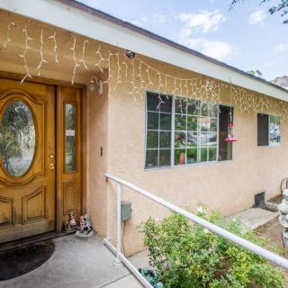 A cozy house exterior with a wooden front door, decorated with string lights above the entrance and a small garden beside the pathway.