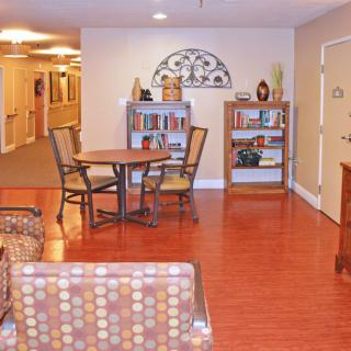 A cozy interior space featuring a wooden floor, shelves with books and decor, a round table with chairs, and comfortable seating.