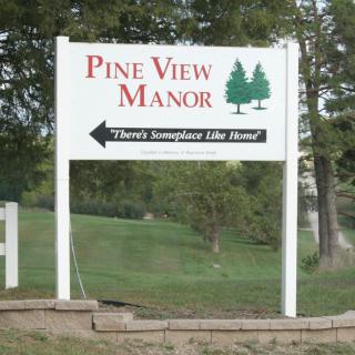 A sign for Pine View Manor with a directional arrow and pine tree graphics.