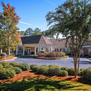 A well-maintained building entrance surrounded by lush greenery and a circular driveway.