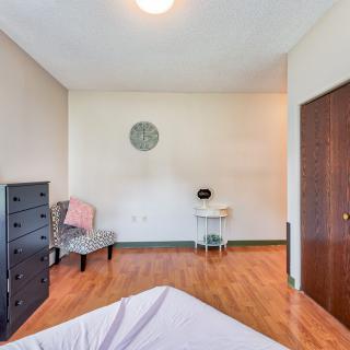 A minimalist bedroom featuring a dresser, chair, and desk with wooden flooring.