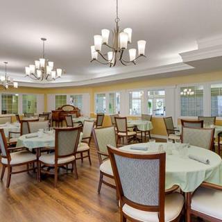 A spacious and elegantly designed dining area with neatly arranged tables and chairs, illuminated by stylish chandeliers.