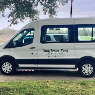 A white van parked on a grassy area under a tree, with 'Sunflower Park' written on the side.