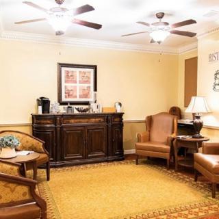A cozy living room with classic decor featuring lounge chairs, a wooden cabinet, and warm lighting.