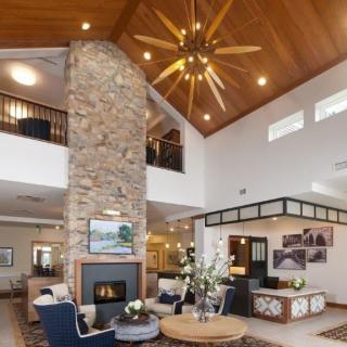 A modern living room featuring a large stone fireplace, high ceilings with a wooden finish, and a stylish chandelier.