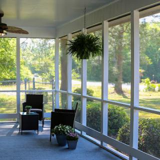 A serene screened-in porch with comfortable seating and hanging plants, inviting relaxation in a sunlit environment.