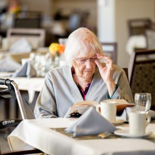 An elderly woman reading at a dining table in a restaurant setting.