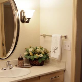 A cozy bathroom with a round mirror, elegant lighting, and decorative flowers on the countertop.