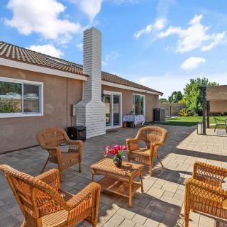 A cozy outdoor patio area with wicker furniture and a chimney, set against a sunny garden backdrop.