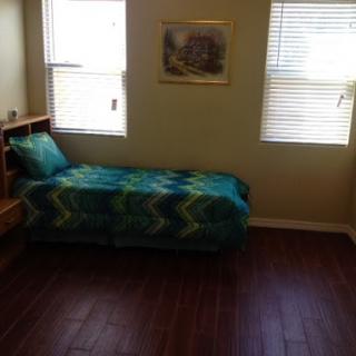 A cozy bedroom featuring a single bed with a colorful blanket and ample natural light from the windows.