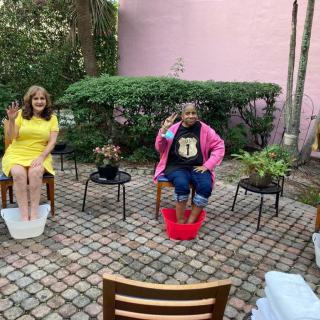 Two people enjoying a relaxing foot bath on a brick patio surrounded by plants.
