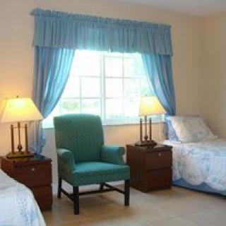 A cozy bedroom with two beds, a chair, and a window with blue curtains.
