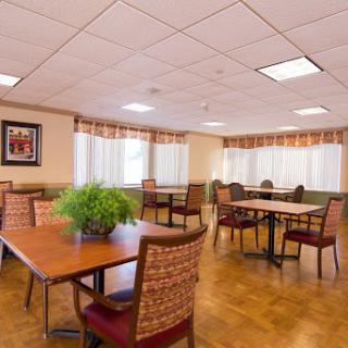 A spacious dining room featuring wooden tables and comfortable chairs, illuminated by natural light through large windows.