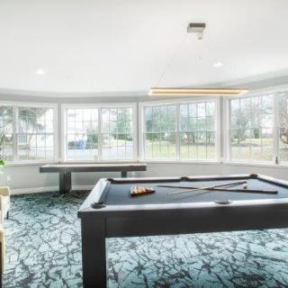 A bright and modern game room featuring a pool table with ample natural light coming through the large windows.