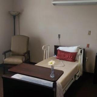 A simple hospital room with a bed, chair, and side table.