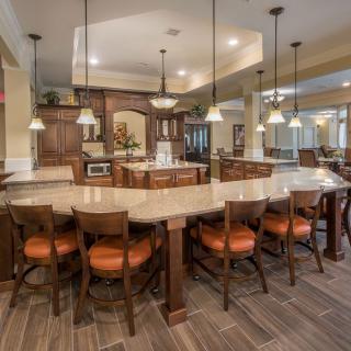 A spacious modern kitchen and dining area with a large curved countertop and multiple chairs, illuminated by pendant lights.