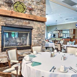 A cozy restaurant dining area with a stone fireplace and elegantly set round tables.