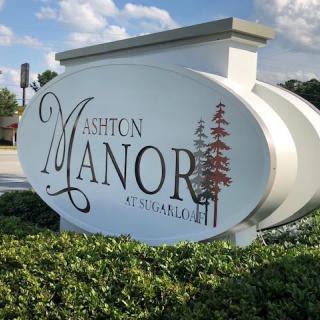 The Ashton Manor sign stands prominently in a landscaped area.
