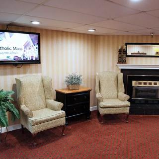 A cozy seating area with two armchairs, a small table, and a fireplace, adjacent to a television mounted on the wall.