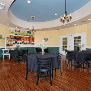 A cozy dining room setup featuring tables and chairs, illuminated by elegant chandeliers, with a bar area in the background.