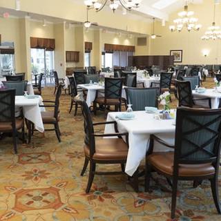 An elegantly designed dining room with neatly arranged tables and chairs, featuring warm lighting and decorative chandeliers.