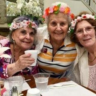 Three elderly women wearing flower crowns enjoy a cheerful gathering.