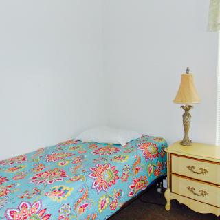A minimalist bedroom with a single bed covered in a colorful bedspread next to a nightstand and lamp.