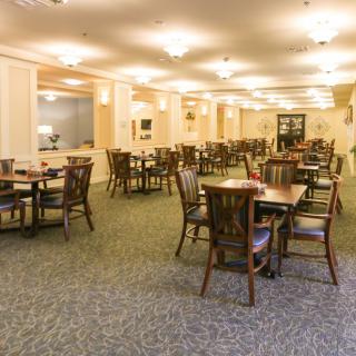 A spacious dining area with multiple tables and chairs arranged neatly, featuring carpeted flooring and warm indoor lighting.