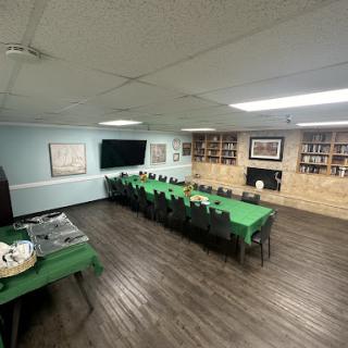 A spacious meeting room set up with a long table covered in green cloths, featuring shelves and a TV on the wall.