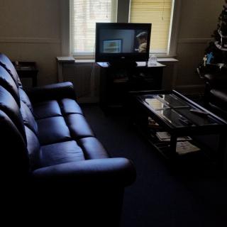A cozy living room with a leather sofa, television, and a glass coffee table near a window.