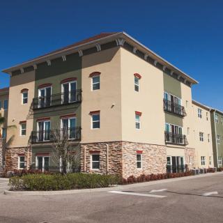 A modern apartment building with a beige and green facade under a clear blue sky.