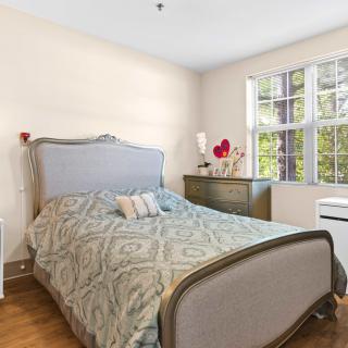 A cozy bedroom with a stylish bed, dresser, and large window allowing natural light.