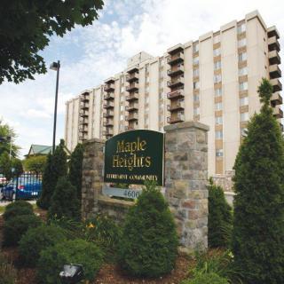 A multi-story residential apartment building with surrounding trees and a prominent sign in the foreground.