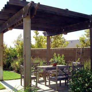 A cozy backyard patio with a wooden pergola providing shade over an outdoor seating area.