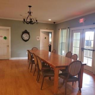 A cozy dining room with a long wooden table and elegant chairs, featuring a decorative chandelier and wall clock.