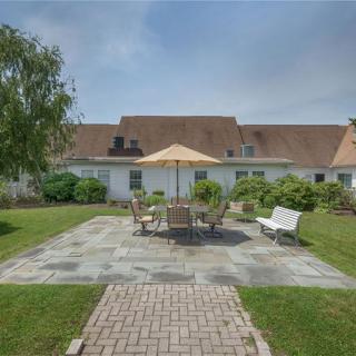 A well-maintained backyard patio with outdoor furniture and an umbrella, surrounded by greenery.