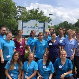 A team of healthcare workers poses for a group photo outdoors in front of a nursing home.