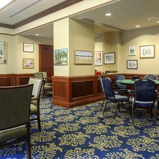 A well-lit room with several tables and chairs, adorned with artwork on the walls and featuring a patterned carpet.