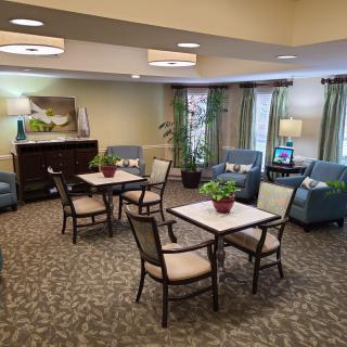 A cozy living room with tables and chairs, decorated with plants and natural lighting.