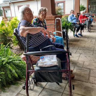Elderly residents enjoying a sunny day outdoors at a care facility, engaged in conversation.
