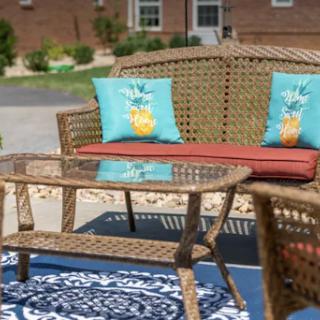 A cozy outdoor seating area featuring a wicker sofa with colorful cushions and a glass-top coffee table, perfect for relaxation.